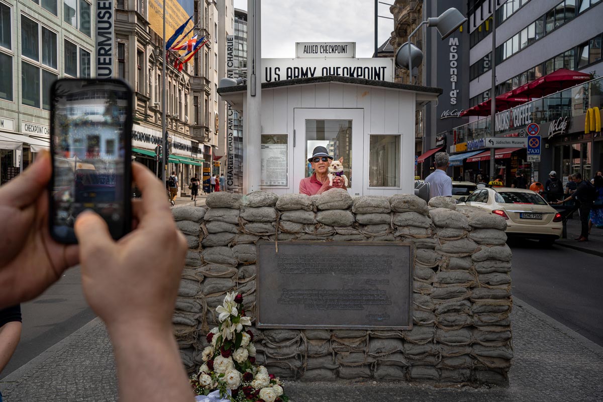 Checkpoint Charlie – A hidegháború idején a legismertebb határátkelő volt Kelet- és Nyugat-Berlin között. A fizikai falból itt szinte semmi sem maradt; a ma látható fehér őrbódé az 1990-es években felállított másolat. A helyszín ma Berlin egyik legforgalmasabb turisztikai pontja, ahol naponta látogatók százai fényképezkednek – itt épp egy férfi kutyáját tartva pózol a poszt előtt Fotó: Szirbek Anita